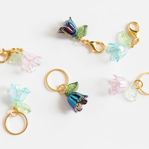 May include: Five flower charms with gold rings and clasps. The flowers are iridescent blue, pink, and green.