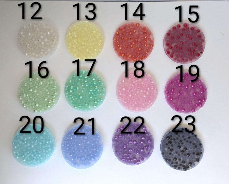 May include: A collection of twelve circular, translucent embellishments, each filled with small, colorful beads. The colors include white, yellow, orange, red, pink, green, teal, blue, purple, and black. Numbers 12 through 23 are printed above each circle.