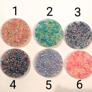 May include: Six round coasters with a textured surface, each filled with small, colorful beads. The coasters are numbered 1 through 6. Colors include pink, blue, purple, and peach.