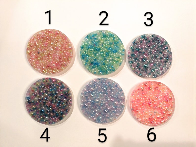 May include: Six round coasters with a textured surface, each filled with small, colorful beads. The coasters are numbered 1 through 6. Colors include pink, blue, purple, and peach.