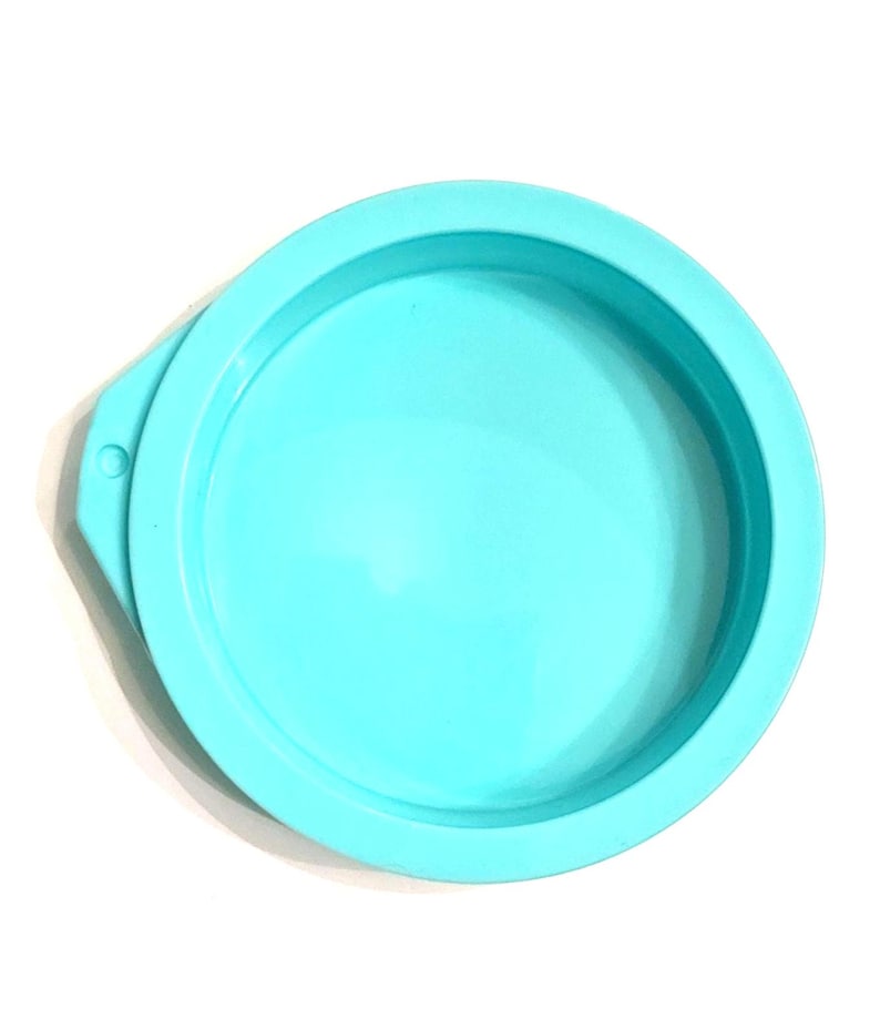 May include: A round, light blue silicone mold with a raised edge and a small tab on the side. The mold is designed for creating round objects and is set against a white background.