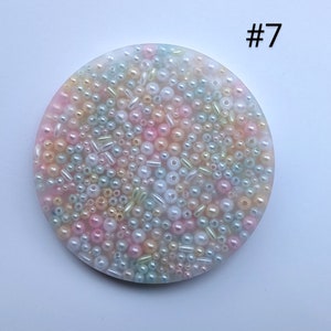 May include: A round, pastel-colored coaster with a multitude of beads and small cylinders in shades of pink, yellow, green, and white. The number "#7" is printed in the upper right corner. The coaster is likely made of resin.
