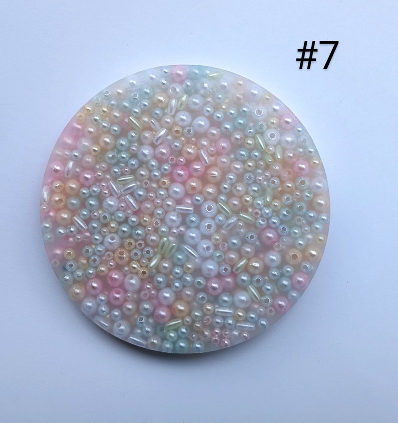 May include: A round, pastel-colored coaster with a multitude of beads and small cylinders in shades of pink, yellow, green, and white. The number "#7" is printed in the upper right corner. The coaster is likely made of resin.
