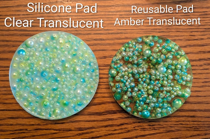 May include: Two round, translucent pads covered in small, colorful beads. One is clear with blue and green beads, the other is amber with green and yellow beads. Text at the top reads "Silicone Pad Clear Translucent" and "Reusable Pad Amber Translucent."