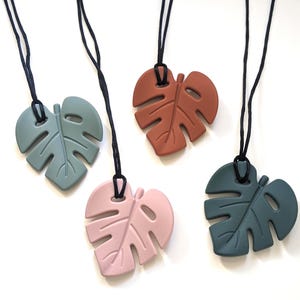 May include: Four silicone necklaces with a monstera leaf design. The necklaces are available in green, pink, brown, and dark green.