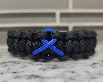 Puede incluir: Pulsera de paracord negra con un diseño de cruz azul. La pulsera presenta un diseño tejido con un acento azul. Este accesorio hecho a mano es una joya elegante y duradera.