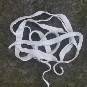 May include: A white, rubbery, flexible strip of material is twisted and knotted into a complex shape on a grey, textured surface.