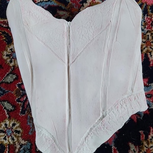 Peut inclure: Un corset en plâtre blanc avec un motif de dentelle. Le corset est un objet décoratif et a une fermeture éclair sur le devant.