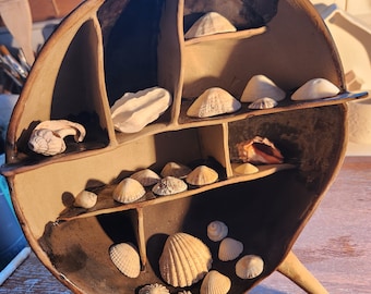 May include: A ceramic seashell display stand with multiple shelves. The stand is brown and black with a rounded top and three legs. The shelves are filled with various seashells.