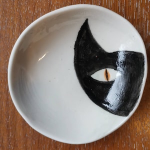 Op de afbeelding: Een witte keramische schaal met een zwart-wit kattenontwerp. Het oog van de kat is oranje geverfd.
