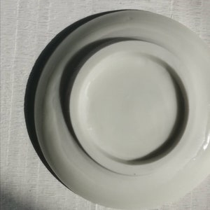 以下が含まれることがあります： わずかに盛り上がった縁のある白いセラミック製の受け皿。受け皿は空で、滑らかで光沢のある仕上げになっています。