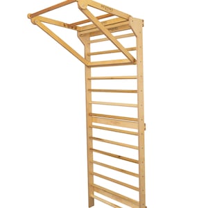 May include: A wooden wall-mounted pull-up bar and climbing ladder with a folding design. The bar is made of natural wood and has a light brown finish. The ladder has 10 rungs and is also made of natural wood. The product is labeled "BEYOND MOVEMENT".
