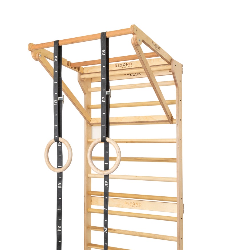 May include: A wooden wall-mounted pull-up bar with adjustable height and two wooden gym rings hanging from black straps. The bar has the text "BEYOND BALANCE" printed on it.