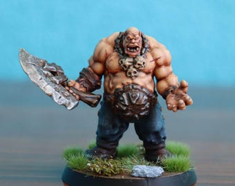 May include: A painted miniature figurine of a muscular humanoid creature with pale skin, wearing dark blue pants and a metal belt. The figure holds a large, weathered silver axe in one hand and wears a necklace adorned with three small skulls.