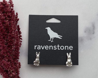 May include: A pair of silver rabbit stud earrings on a black card with the text "ravenstone" and a silhouette of a raven.