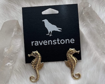 May include: A pair of gold-tone seahorse earrings on a black card with the word "ravenstone" printed in white.