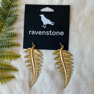 May include: Gold fern leaf earrings with a black card that says "ravenstone" and a silhouette of a raven.