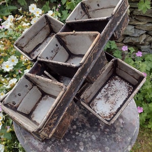 May include: A set of five vintage metal bread loaf tins. The tins are stacked and angled, showing their worn, white enamel finish with brown rust spots.