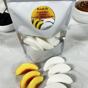 Puede incluir: Una bolsa plateada etiquetada "The Candle Chef" que contiene modelos de rodajas de melocotón blancas para moldes de silicona DIY. Se muestran varias rodajas de melocotón amarillas y rojas y modelos de rodajas de melocotón blancas.