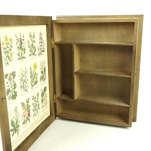 May include: A wooden cabinet with a glass door and shelves. The door has a botanical print with illustrations of various flowers and plants.
