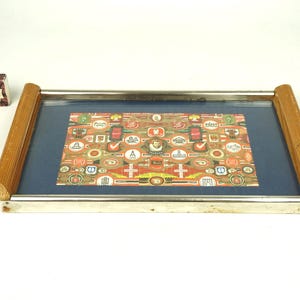 Peut inclure: Plateau de service rectangulaire avec un intérieur bleu et une impression décorative. Le plateau a un cadre en métal argenté et des poignées en bois. Une petite boîte avec le mot "ZOZIOZ" est à côté du plateau.