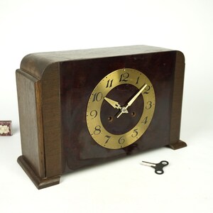 May include: A vintage wooden clock with a dark brown finish and a gold face. The clock has a key wind mechanism and is in good condition.