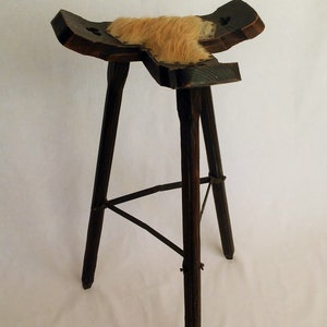 May include: A wooden stool with a fur seat and three legs. The legs are connected by a metal brace.