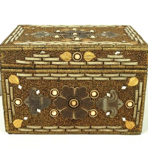May include: A decorative rectangular box with a hinged lid. The box is covered in small, gold-colored beads and accented with silver and gold-colored floral and leaf designs. The box has a rectangular shape and is likely used for storage.