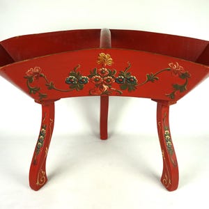 Peut inclure: Un bol en bois rouge avec des motifs floraux peints et trois pieds. Le bol est en forme de croissant de lune et a un intérieur profond et arrondi.