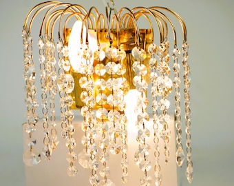 May include: A gold-toned wall sconce with crystal beads hanging down in a waterfall design. The sconce has two light bulbs.