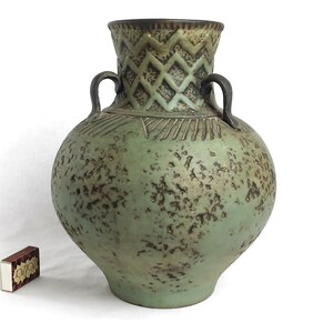 May include: A large, green ceramic vase with two handles and a textured surface. The vase has a geometric design around the neck.