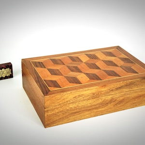 May include: A wooden box with a geometric pattern on the lid. The lid is made of different types of wood, creating a 3D effect. The box is closed.