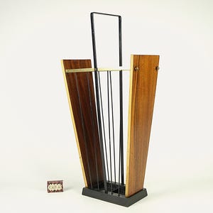 May include: A mid-century modern umbrella stand with a black base and frame. The stand features wooden panels with brass accents and black rods for holding umbrellas. The design is a mix of wood and metal.
