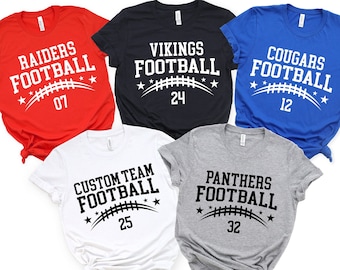 May include: Five different t-shirts with a football theme. The shirts are red, navy blue, royal blue, white, and heather gray. Each shirt has a different team name and number printed on the front. The text on the shirts reads "RAIDERS FOOTBALL 07", "VIKINGS FOOTBALL 24", "COUGARS FOOTBALL 12", "CUSTOM TEAM FOOTBALL 25", and "PANTHERS FOOTBALL 32".
