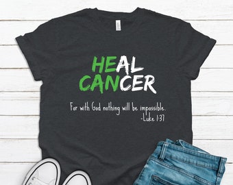 Op de afbeelding: Een donker antracietgrijs T-shirt met korte mouwen en de tekst HEAL CANCER in groene en witte penseelstreekletters. Onder de tekst staat het wit gedrukte citaat: For with God nothing will be impossible. -Luke 1:37.