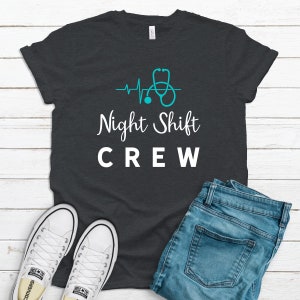 May include: A dark gray t-shirt with a white graphic that says "Night Shift Crew" and a blue stethoscope with a heartbeat line.