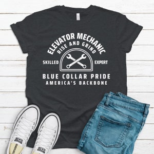 May include: A dark grey t-shirt with white text that reads "Elevator Mechanic Rise and Grind Skilled Expert Blue Collar Pride America's Backbone". The text is in a circular design with a graphic of two crossed spanners.