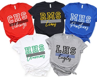 May include: Five short-sleeved t-shirts in red, black, blue, white, and gray. Each shirt features a school name and mascot design in bold lettering. The shirts are for the Vikings, Lions, Panthers, Warriors, and Eagles.