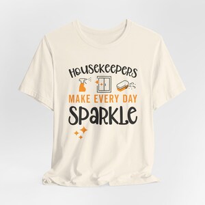 Natural colored graphic t-shirt with cleaning icons that says Housekeepers Make Every Day Sparkle