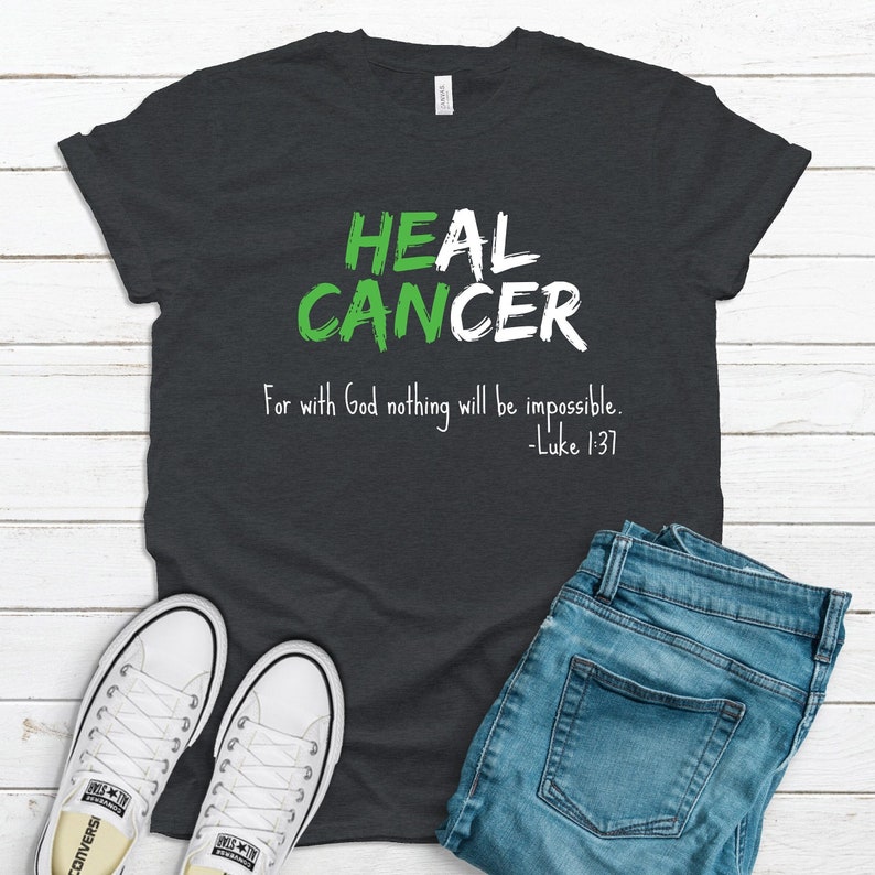 Dark gray heather graphic t-shirt that says He Can Heal Cancer - For With God Nothing Will Be Impossible - Luke 1:37. The design is in green and white.