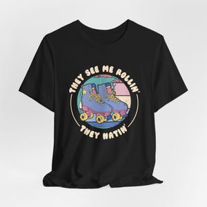 Black graphic t-shirt with retro roller skate design that says They See Me Rollin They Hatin