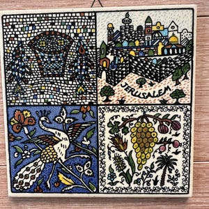 Könnte beinhalten: Quadratische Keramikfliese mit vier illustrierten Tafeln. Die Tafeln zeigen einen mosaikartigen Torbogen, eine Stadtlandschaft mit "Jerusalem", einen Pfau und Trauben. Die Fliese hat einen Aufhänger. Maße in Zentimetern.