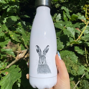 Pu&ograve; includere: Borraccia termica bianca con coperchio argentato. La borraccia presenta una dettagliata illustrazione in bianco e nero di una lepre. &Egrave; progettata per mantenere le bevande fredde fino a 24 ore e calde fino a 12 ore.