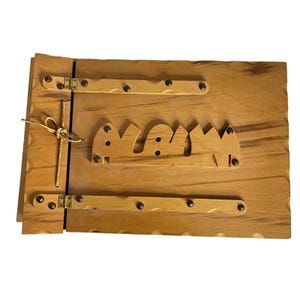 Op de afbeelding: Een rechthoekig houten fotoalbum met een lichtbruine houtnerfafwerking. De kaft bevat het woord "ALBUM" in uitgesneden houten letters, twee horizontale houten strips bevestigd met metalen scharnieren en studs, en een decoratief touwtje.