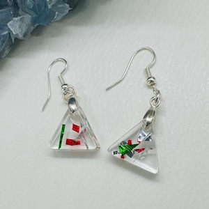 May include: Clear, triangular earrings with silver hooks. Each earring features red, green, and silver foil accents encased in clear resin. The earrings are designed for pierced ears and are displayed on a white surface.