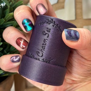 May include: A set of three ceramic mugs with a speckled, cream-colored glaze. Each mug features a different hand-painted design: a blue and green leaf, a yellow flower, and a red berry. The mugs have a simple, modern design.