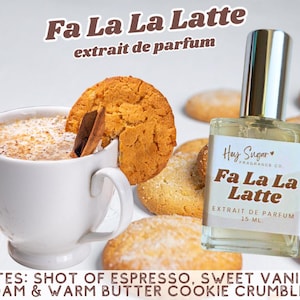 May include: A perfume bottle labeled "Fa La La Latte" sits next to a white mug of latte with a cinnamon stick and a cookie. The image includes cookies and text that reads "extrait de parfum" and "15 ML."