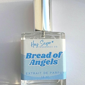 May include: A clear glass perfume bottle with a silver cap. The label reads "Hey Sugar Fragrance Co." and "Bread of Angels" in blue text. The bottle contains 15 ml of perfume.