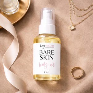 May include: A clear glass bottle of "Bare Skin" body oil with a white label and a pump dispenser. The label includes the text "hey SUGAR FRAGRANCE CO." and "2 oz." A gold necklace with a heart pendant and a gold ring are also visible.