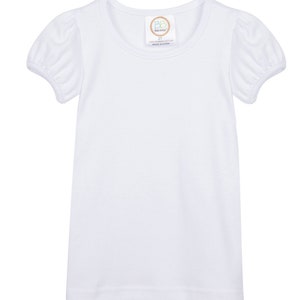 May include: White short-sleeved t-shirt with a round neckline and puffed sleeves. The shirt has a small tag with the text "Baby Boutique 2T 100% Combed Cotton Made in China" on the front.